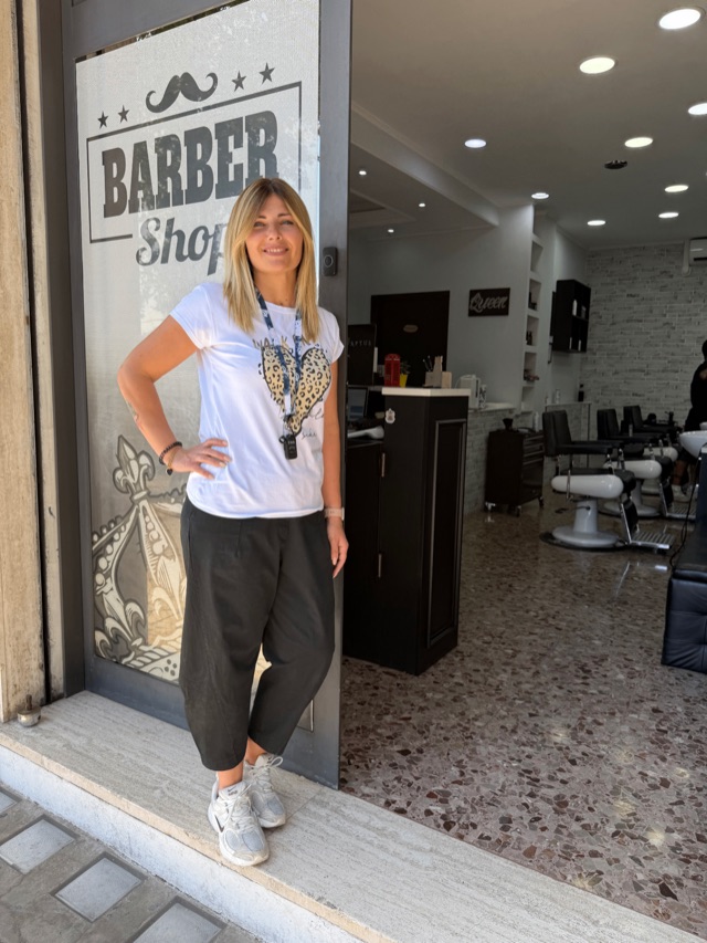 Veronica sulla soglia del salone Queen, in maglietta bianca, sorridente